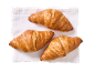 Trois croissants dorés sur une serviette en lin blanc.
