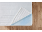 Matelas blanc en mousse, partiellement ouvert sur un sol en bois.