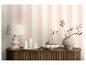 Meuble en bois avec lampe, bougies et vase décoratif devant un mur rayé rose et blanc.