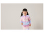 Une fille porte un survêtement rose et bleu avec un motif arc-en-ciel.