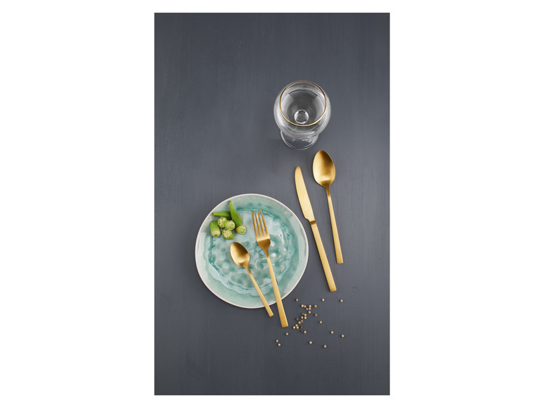 Des couverts dorés, une assiette et un verre sur un fond gris.