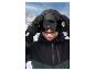 Un homme avec un casque et des lunettes de ski noirs sur un fond de montagne.