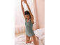 Femme souriante en débardeur et culotte vert sauge, s'étirant sur un lit.