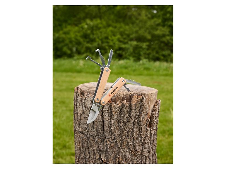 Outil multifonction avec manche en bois et divers accessoires sur une souche d'arbre.