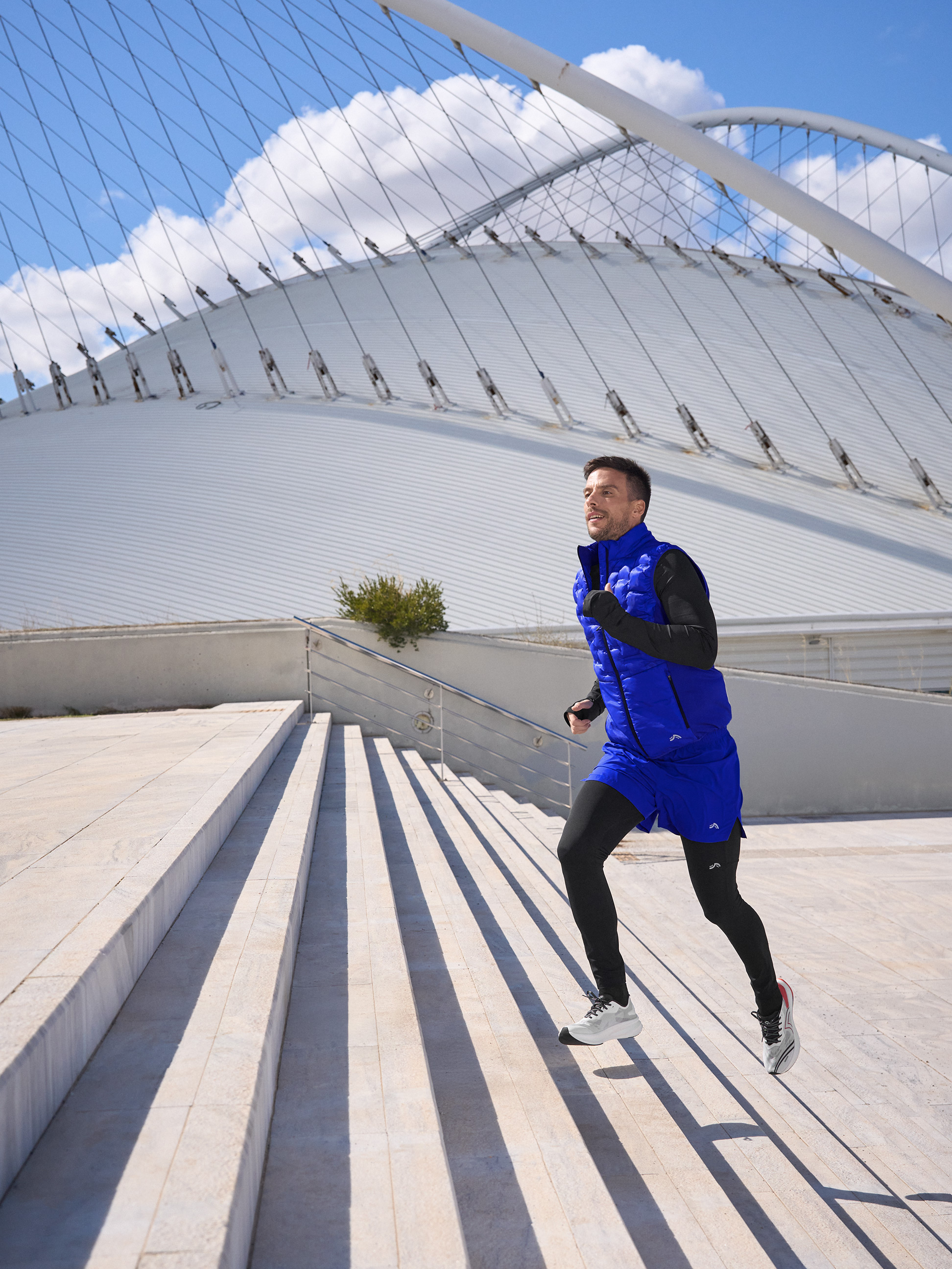 Homme en gilet de course bleu et collants noirs montant des escaliers.