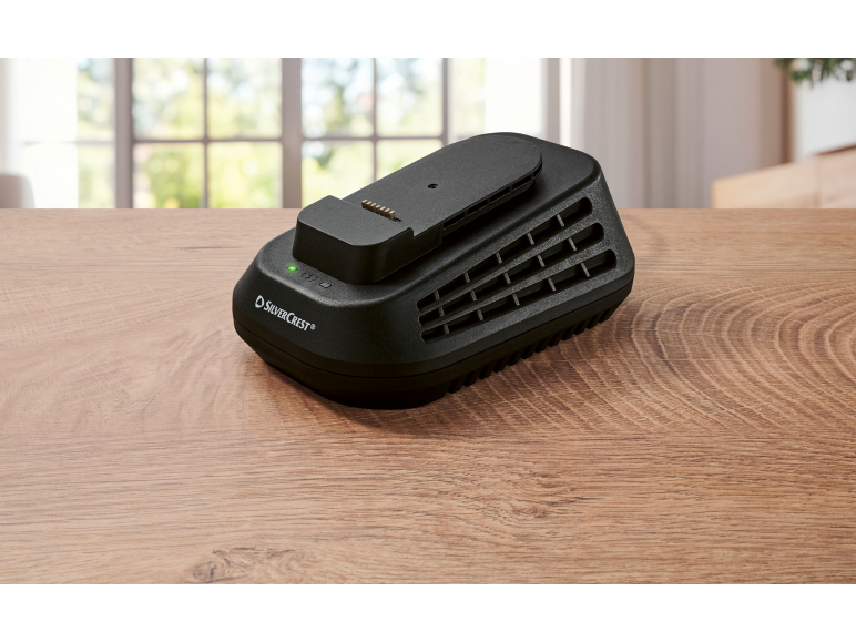 Chargeur de batterie noir avec voyant vert sur une table en bois.