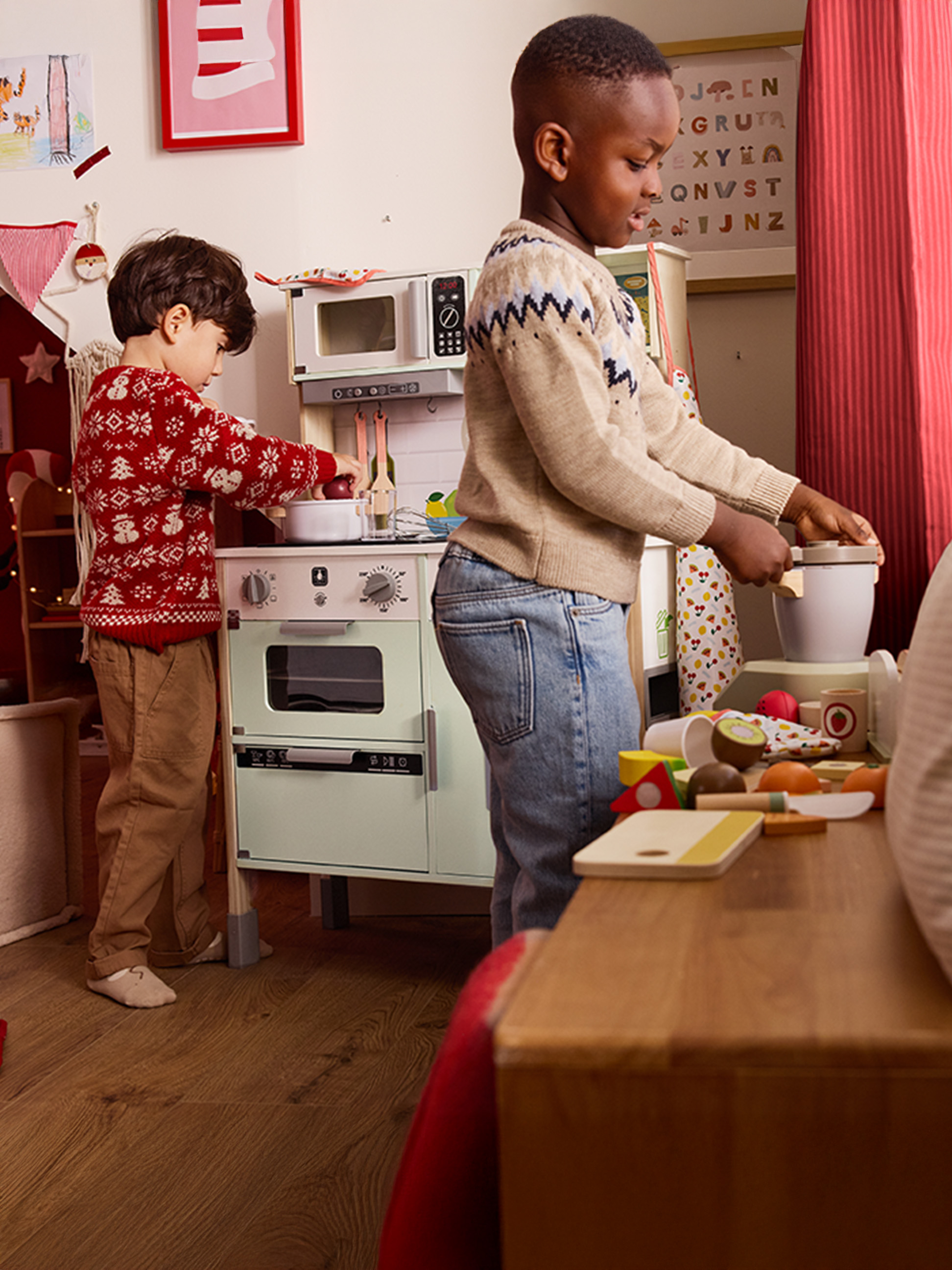 Deux enfants jouent avec une cuisine et des aliments jouets dans une pièce décorée de fête.