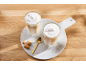 Deux verres de latte macchiato en couches avec de la mousse, une cuillère dorée et des biscuits sur une planche en marbre.