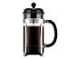 Cafetière à piston avec café foncé et marc, couvercle et poignée noirs, et un cadre chromé.