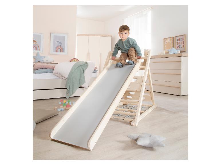 Enfant sur un toboggan en bois dans une chambre d'enfant sur le thème de l'arc-en-ciel.