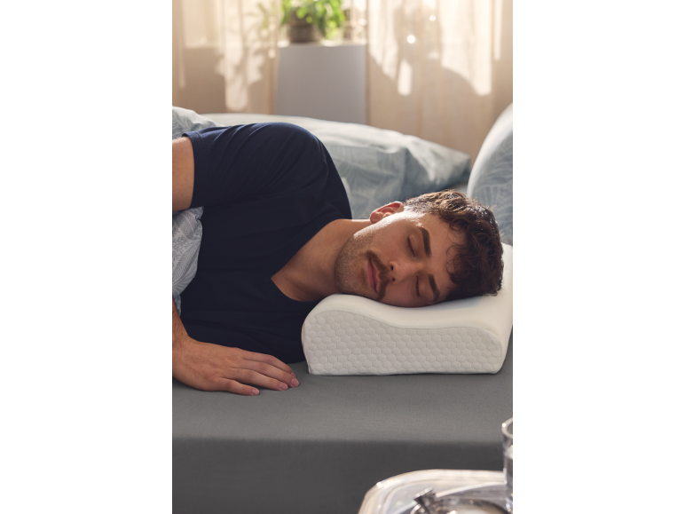 Homme dormant sur le côté sur une literie grise, la tête sur un oreiller ergonomique.