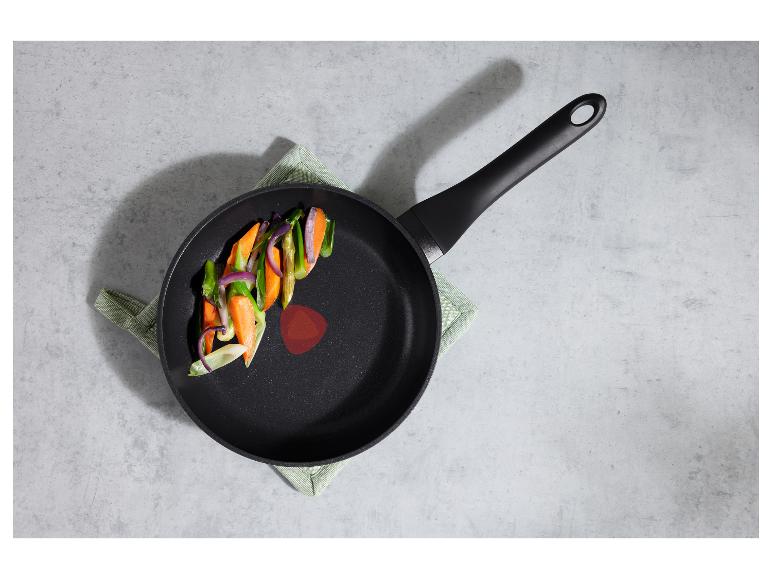 Poêle avec des légumes sur une surface grise avec un torchon vert.