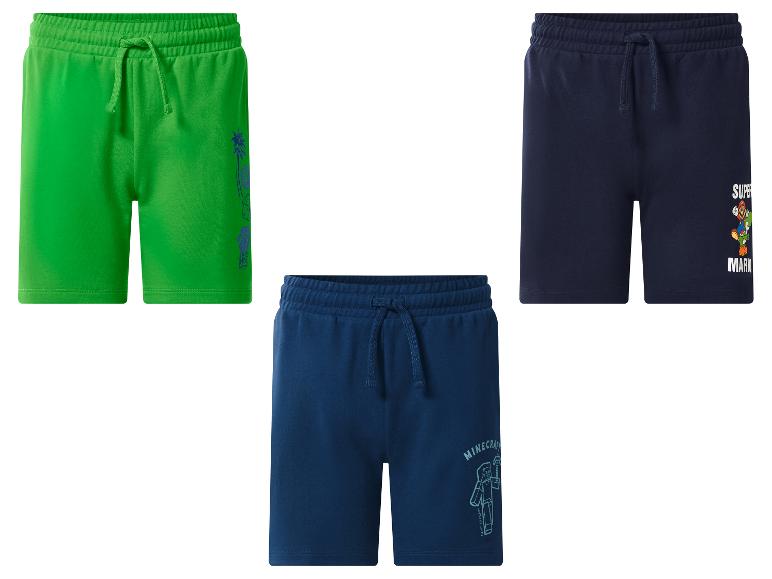 Trois shorts pour enfants: vert avec motif palmier, bleu foncé avec Super Mario et bleu foncé avec Minecraft.