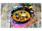 Paella aux fruits de mer dans une poêle noire avec couvercle en verre, sur une table en bois avec un torchon à carreaux.