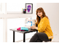 Femme souriante avec machine à coudre et tissus colorés sur une table.