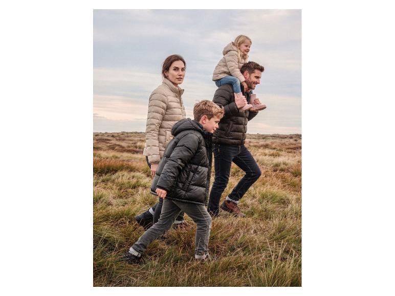 Famille en doudounes et chaussures robustes marchant dans un paysage herbeux.