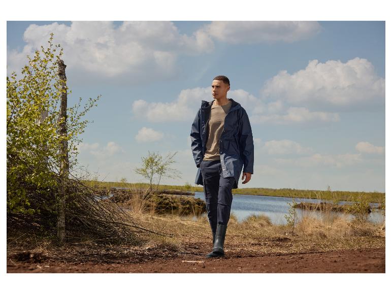 Homme en veste imperméable bleu foncé et pantalon cargo, marchant sur un chemin boueux.