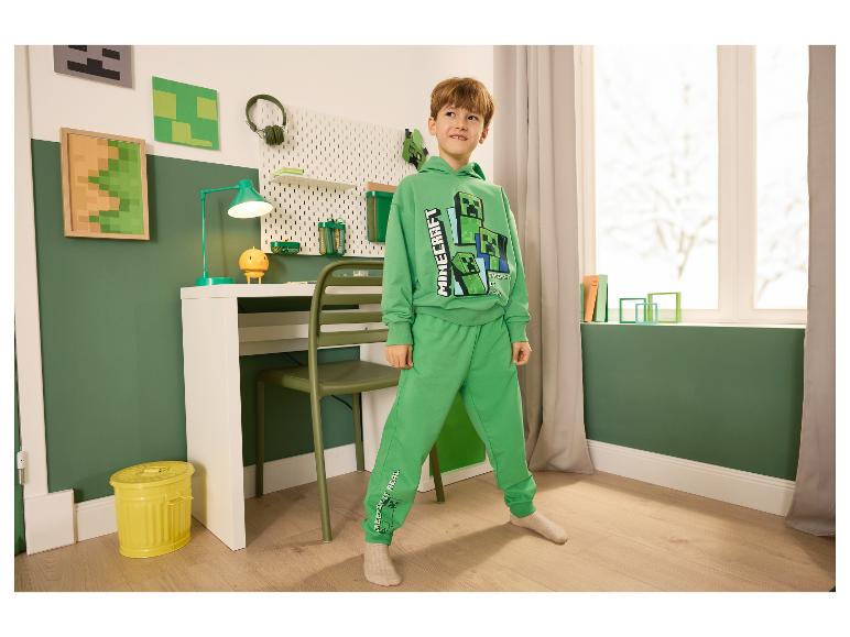 Garçon en survêtement vert Minecraft dans une chambre à la décoration thématique.