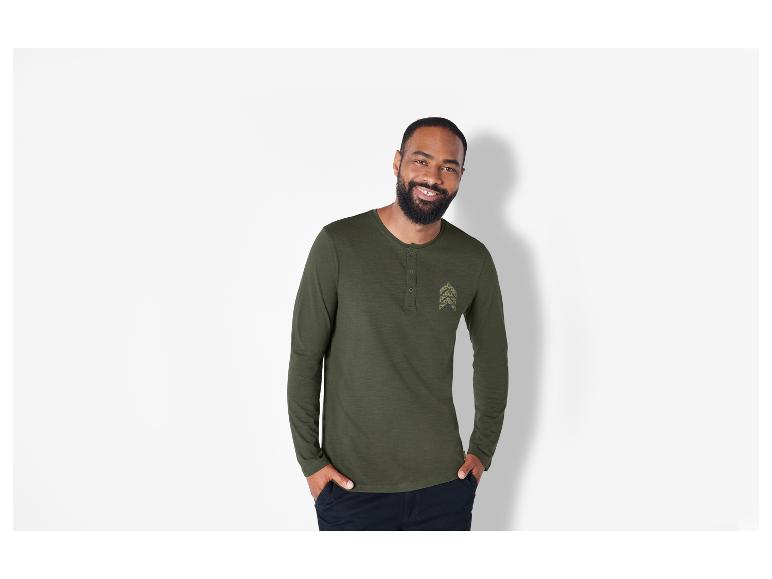 Un homme porte un Henley à manches longues vert avec un petit logo.