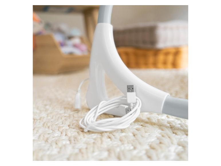 Câble USB blanc et chargeur sur un tapis blanc, avec des objets flous en arrière-plan.