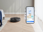 Aspirateur robot noir sur parquet à côté d'un smartphone avec une application de contrôle.