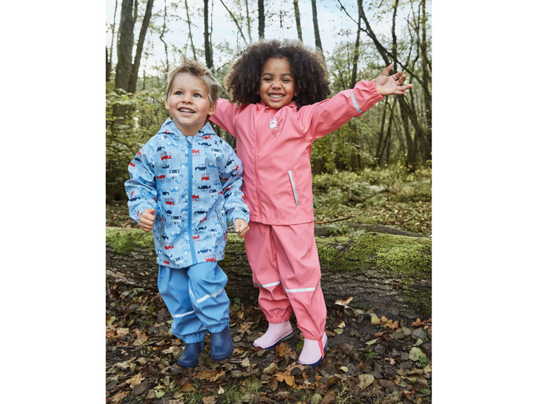 Deux enfants en vêtements de pluie, un garçon dans un imperméable bleu avec des voitures et une fille dans un pantalon de pluie rose