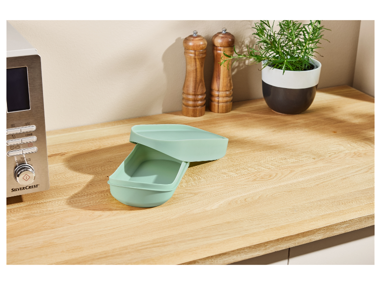 Four à micro-ondes SilverCrest et boîte repas en silicone vert clair sur un comptoir en bois.