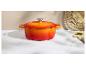 Cocotte en fonte orange-rouge sur un comptoir en marbre blanc avec une planche à découper et un couteau.