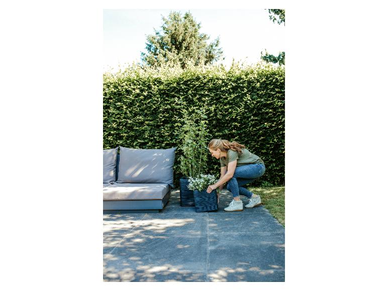 Femme plantant des fleurs en pots sur une terrasse avec mobilier de jardin.