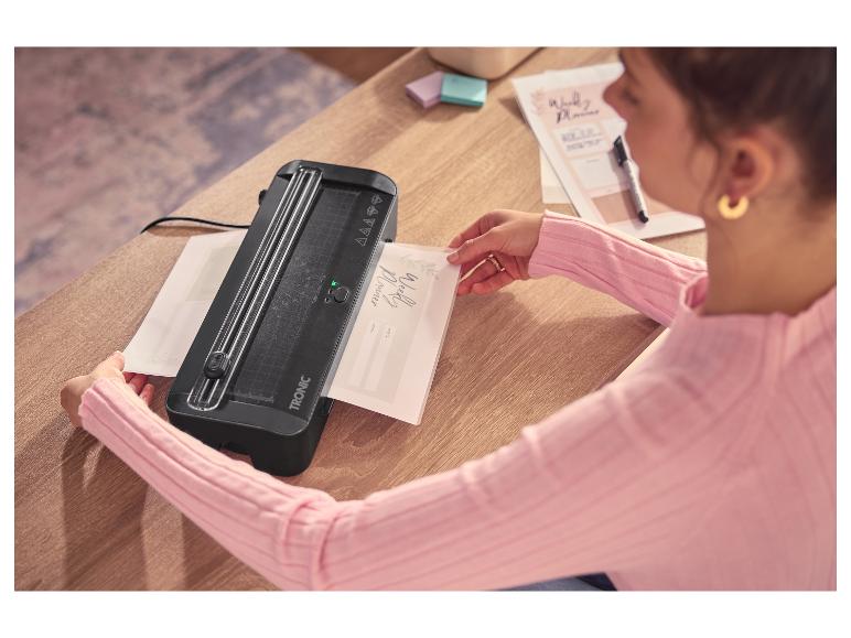 Femme laminant un agenda hebdomadaire avec une plastifieuse sur une table en bois.