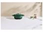 Cocotte en fonte verte avec couvercle, herbes et salière-poivrière sur un comptoir en marbre.