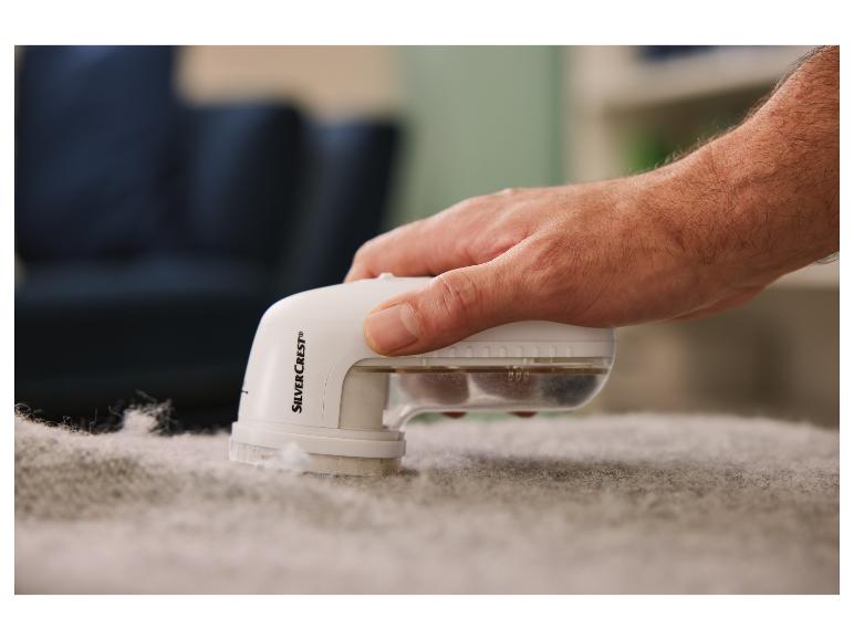 Une main tenant un rasoir électrique SilverCrest pour enlever les peluches du tissu.