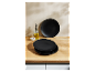 Assiettes noires empilées sur une surface en bois, à côté d'une bouteille d'huile et d'un bol de sel.