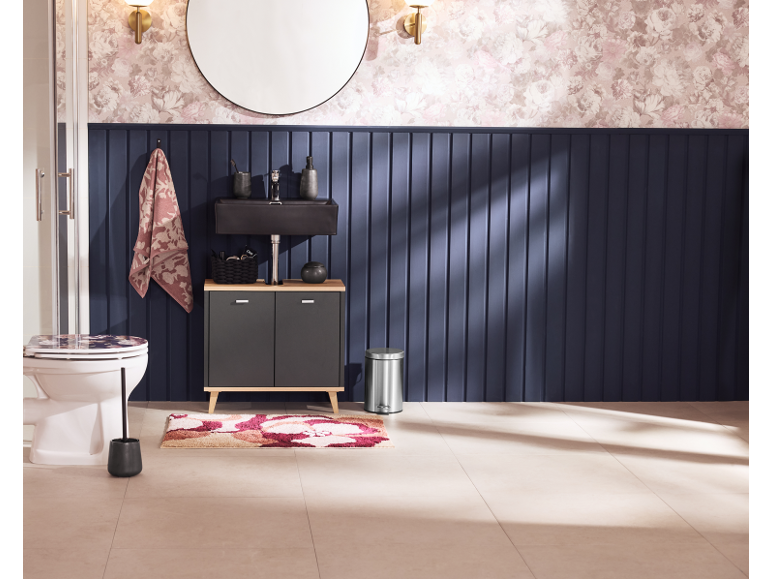Salle de bain avec meuble-lavabo noir, toilettes, tapis floral et mur lambrissé bleu marine.