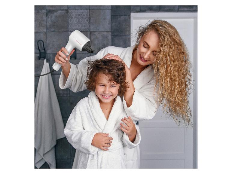 Femme séchant les cheveux d'un enfant avec un sèche-cheveux, tous deux en peignoir.