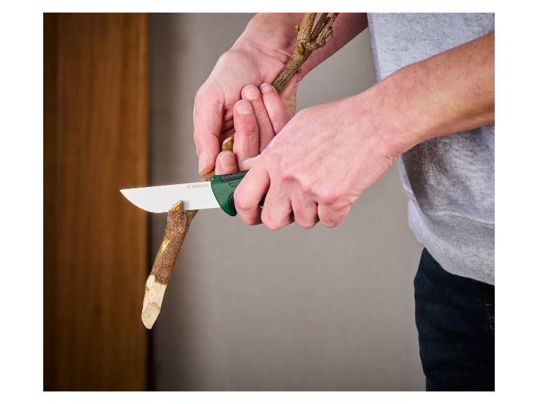 Des mains coupent une branche avec un couteau Parkside.