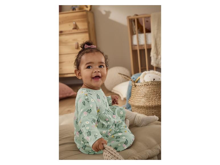 Bébé joyeux en robe fleurie assis sur un coussin dans une chambre d'enfant.