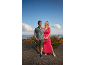 Homme en polo et short, femme en robe longue, tous deux souriants en extérieur.