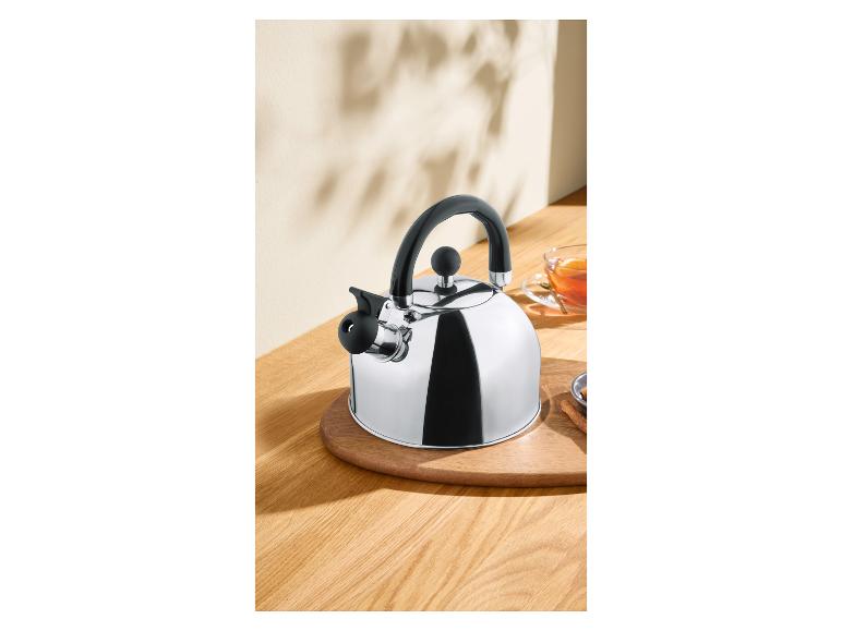 Bouilloire à thé en métal brillant avec poignée noire sur une table en bois avec une tasse de thé.