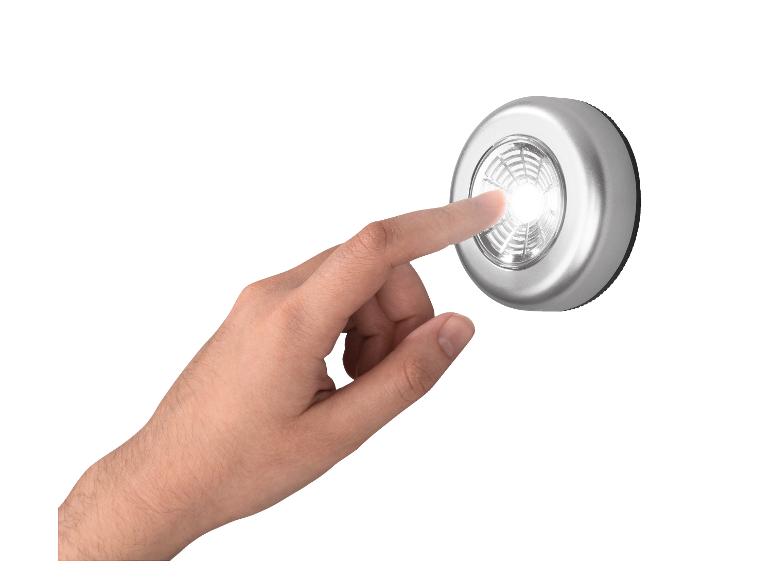 Main appuyant sur une lumière LED argentée allumée sur fond blanc.