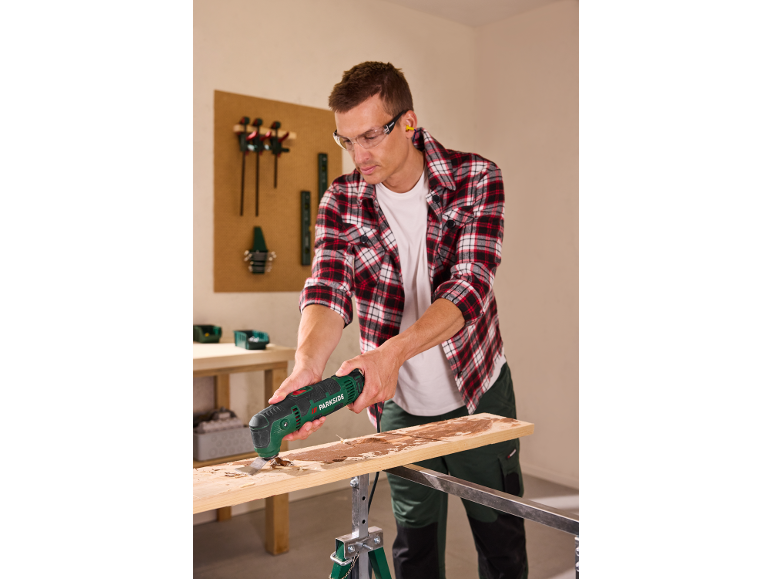 Homme utilisant un outil multifonction pour racler du bois, portant des lunettes de sécurité et des bouchons d'oreille.