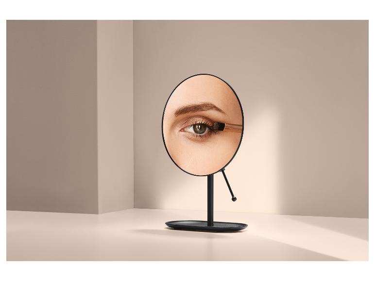 Miroir avec un œil de femme appliquant du fard à paupières, sur fond clair.
