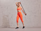 Femme en soutien-gorge de sport et leggings orange utilisant une bande de résistance.
