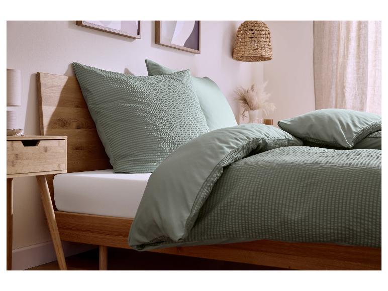 Chambre avec cadre de lit en bois, housse de couette et oreillers vert sauge texturés gaufrés.