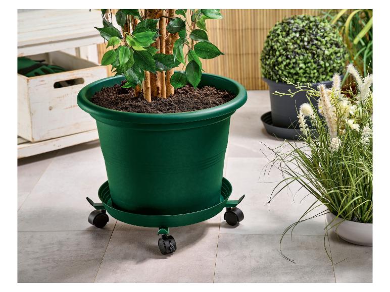 Grande plante artificielle dans un pot vert sur un support à roulettes, à côté d'autres plantes.