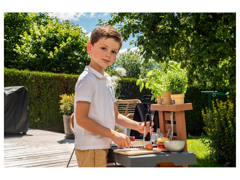 Un garçon joue avec un barbecue et des ustensiles de cuisine en plastique.