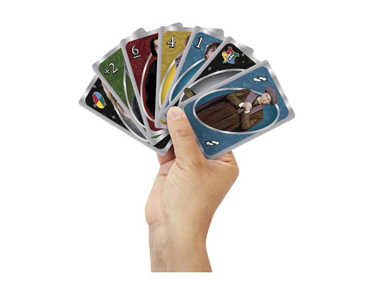 Main tenant un éventail de cartes à jouer sur le thème de Harry Potter, avec des personnages et des symboles de maisons.