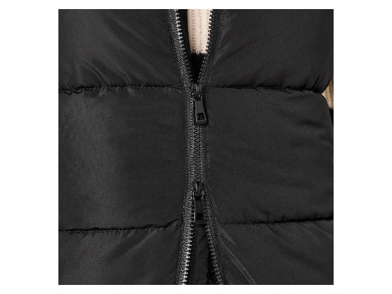Gros plan d'un gilet matelassé noir avec une fermeture éclair partiellement ouverte, révélant un pull en tricot crème.