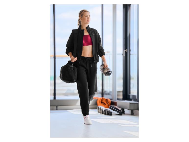 Femme portant une veste de sport CRIVIT, un sac de sport et une gourde.