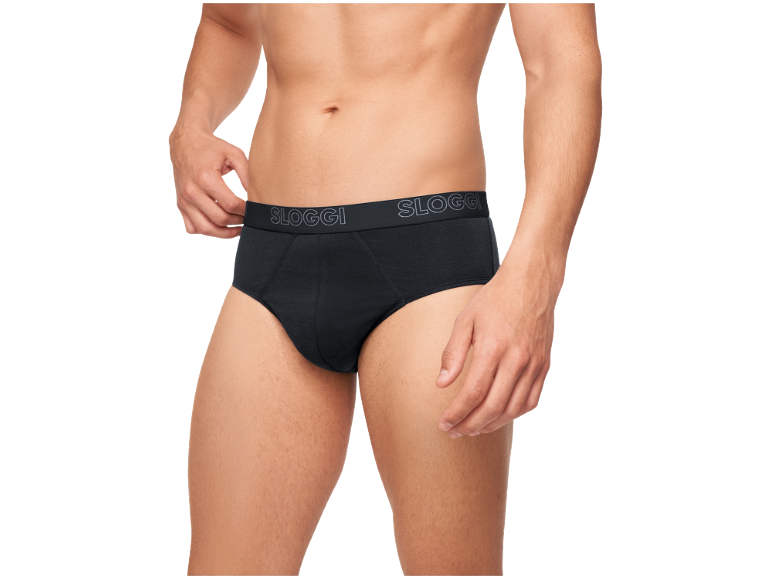 Homme en slip noir, ajustant la taille avec sa main.